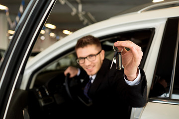 Fototapeta na wymiar Man driver smiling holds car keys in car showroom