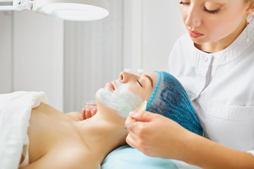 Obraz na płótnie Canvas Cosmetologist makes beauty mask to a young woman.