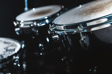Closeup view of a drum set in a dark studio. Black drum barrels with chrome trim. The concept of live performances