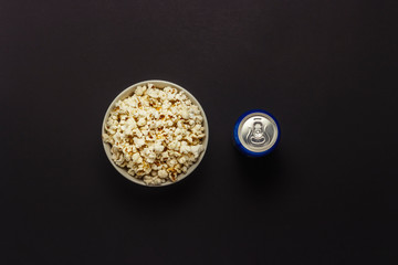 Bowl with popcorn and a can of drink on a black background. The concept of watching movies and favorite TV shows, sports competitions. Flat lay, top view