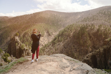 Fototapeta premium Portrait from the back of a traveling girl taking pictures of an epic landscape with rocks on her smartphone