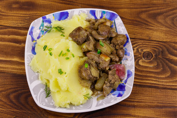 Mashed potatoes with stewed chicken liver with apple and onion on wooden table