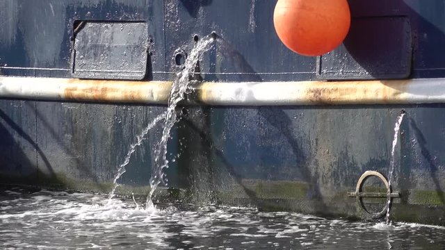 Jets of water from the holes in the blue Board of a metal fishing ship. Marine engine cooling system