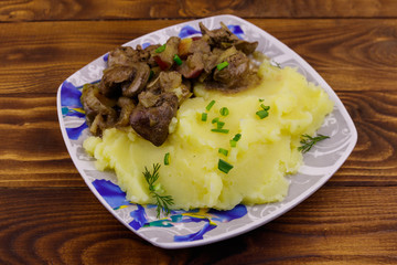 Mashed potatoes with stewed chicken liver with apple and onion on wooden table