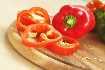 Red and green bell peppers on wooden cutting board.