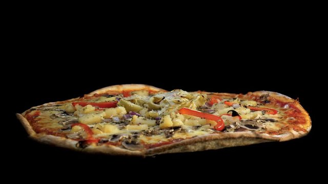 A freshly baked vegetarian pizza rotates against black background