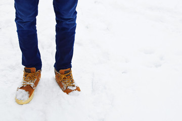Young man legs wearing blue jeans and yellow boots standing on snow outdoors at cold winter day with copy space for text.