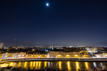 Fototapeta premium Grenoble, France, January 2019 : City at night with isere river, the moon and stars in the sky