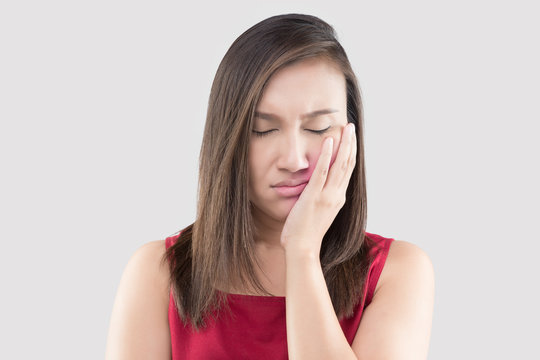 Suffering from a toothache, Asian woman wearing a red shirt suffering from a toothache while standing against a grey background, Teeth Problem, The concept of healthy gums and teeth, Jaw pain