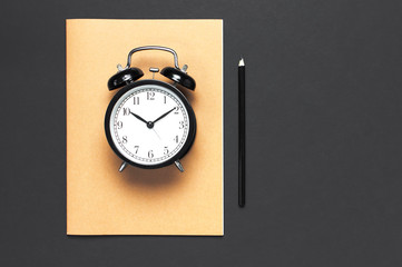 Flat lay black alarm clock, exercise book notebook diary, pencil on gray dark background top view copy space. Concept time to work, desktop, Office desk, Minimalistic background for blog