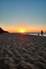 Fototapeta na wymiar dawn. young man with a dog running along a sandy beach