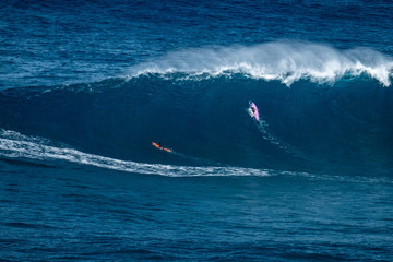 Two big wave surfers paddle to line up and pass huge ocean wave of Jaws (Peahi) surf spot on Maui,...