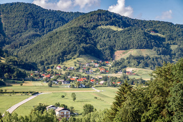 Fototapeta na wymiar Amazing panoramic landscape in Slovenia countryside in a sunny summer day. The meadow, fields and green mountains, the village at the foot of the mountain. Travel Slovenia.