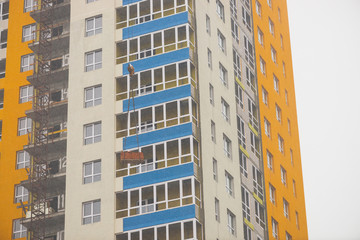 Concept of apartment building under construction close-up. Exterior of multicolor new multi-story residential building. Background with yellow walls, white plastic windows and blue loggias. Copy space