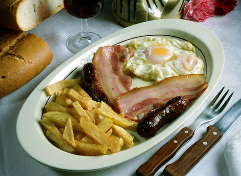 Plato con un huevo frito, dos trozos de beicon, 2 morcillas y patatas fritas.