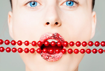 Creative portrait of woman face with closeup bright lips and red pearls. Perfect female mouth with glitter lipstick makeup