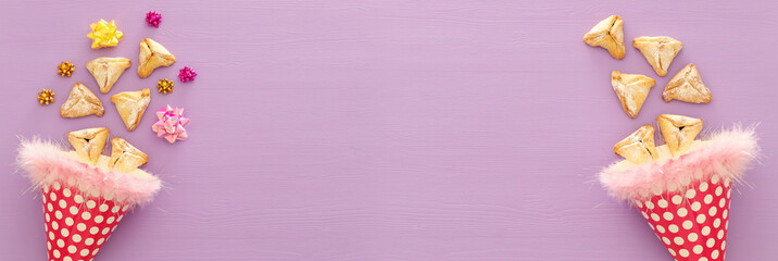 Purim celebration concept (jewish carnival holiday). Traditional hamantaschen cookies over purple wooden table.