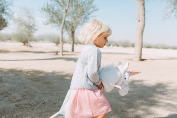 Beautiful little girl in colorful dress riding on wooden toy horse unicorn outdoors .. © TY Studio