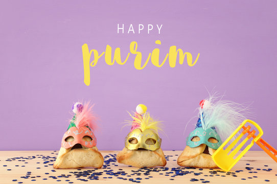 Purim celebration concept (jewish carnival holiday). Traditional hamantaschen cookies with cute clown hats and masks over wooden table.