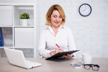 cheerful mature business woman making paperwork in office
