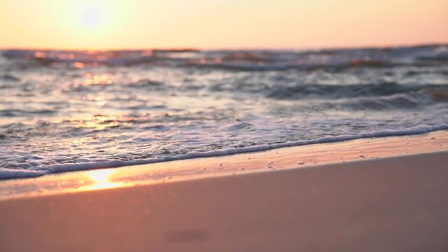 Sunset on the beach. Slow motion footage of sea waves and foam. Sun reflecting on the water surface.