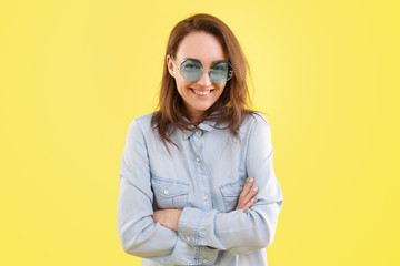 Beautiful young positive woman in a stylish shirt and glasses is smiling and looking into the camera on a yellow background. Advertising space
