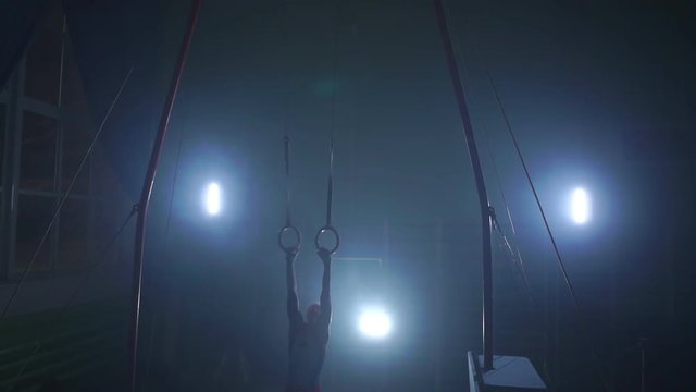a Still shot of a guy working out on the still rings a gymnastics apparatus that is extremely hard in slow motion 180 fps.