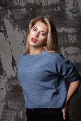 Stunning blonde model with lush hair wearing blue sweater, posing in studio with shadows