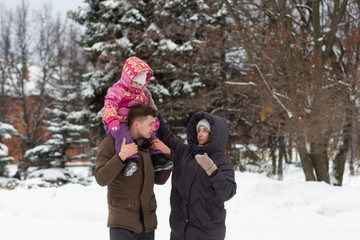 Fototapeta na wymiar Young parents and child sitting on shoulders walking in snowy park