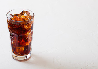 Glass of cola soda drink with ice cubes and bubbles on stone kitchen table background.