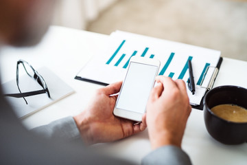 A midsection of businessman sitting at the table, using smartphone. Copy space.