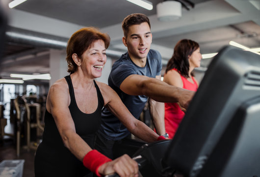 Two cheerful female seniors in gym with a young trainer doing cardio work out.