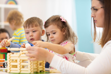 Children and nursery teacher building toy house in a kindergarten