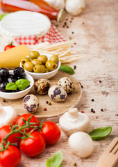 Homemade spaghetti pasta with quail eggs with bottle of tomato sauce and cheese on wooden background. Classic italian village food. Garlic, champignons, black and green olives, oil and spatula.