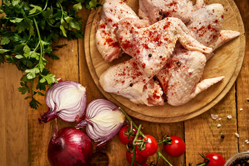 Fresh organic chicken wings on a chopping board with spices and vegetables on wooden table.