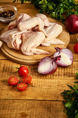 Fresh organic chicken wings on a chopping board with spices and vegetables on wooden table.