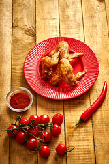 Delicious grilled chicken wings on red plate with spices and tomatoes and chilly peppers on table.