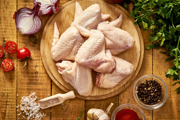 Fresh organic chicken wings on a chopping board with spices and vegetables on wooden table.