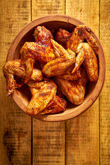 Delicious grilled chicken wings in wooden bowl on wooden table.