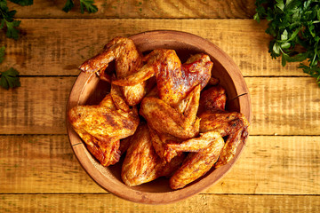 Delicious grilled chicken wings in wooden bowl with parsley on wooden table.