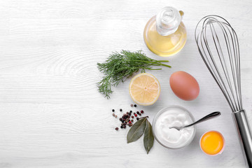 Mayonnaise in a glass bowl and ingredients for making mayonnaise on a white wooden background....