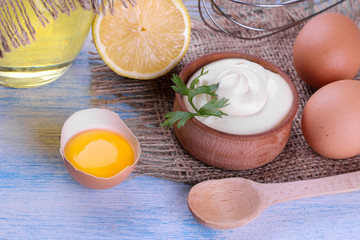 Mayonnaise in a wooden bowl and ingredients for making mayonnaise on a blue wooden background. white sauce.
