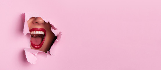 Bright red lips through torn pink paper background. Surprised girl, emotions. Make up artist,...