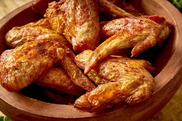 Close up of delicious grilled chicken wings in wooden bowl on wooden table.