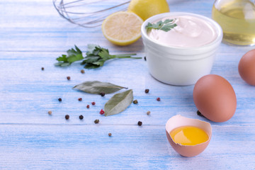 Mayonnaise in a white bowl and ingredients for making mayonnaise on a blue wooden background. white sauce.