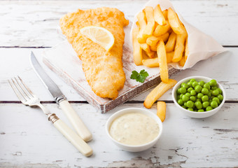Traditional British Fish and Chips with tartar sauce on chopping board with fork and knife and...