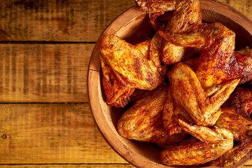 Delicious grilled chicken wings in wooden bowl on wooden table.