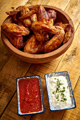 Delicious grilled chicken wings in wooden bowl with dips to choose from on wooden table.