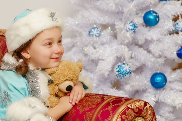 Little girl in the snow maiden costume with a teddy bear near th