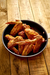 Delicious grilled chicken wings on cast-iron pan on wooden table.